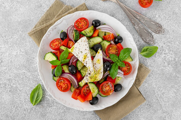 Greek salad of fresh juicy vegetables, feta cheese, herbs and olives on a white plate on a light...