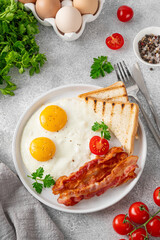 Breakfast with fried eggs, bacon and toasts on a white plate with cup of coffee on a stone background. Top view, selective focus.