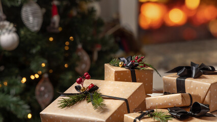 Wrapped Christmas gifts with black bow against burning fireplace and christmas tree lights
