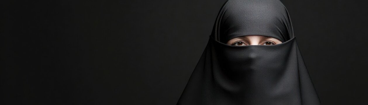 Woman wearing a black niqab, focused expression on a dark background.