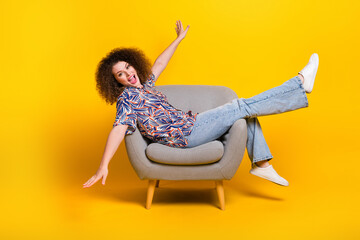 Full length photo of lovely young lady sit armchair spread hands fly have fun dressed colorful...