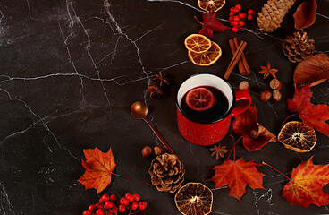Red enamel mugs with hot autumn drink, mulled wine and autumn fallen leaves, star anise, pine cones, rowan and cinnamon on marble table, banner, autumn welcome concept,