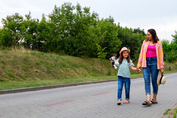 Young woman and her little girl are walking along the road. Mother and daughter are walking together.