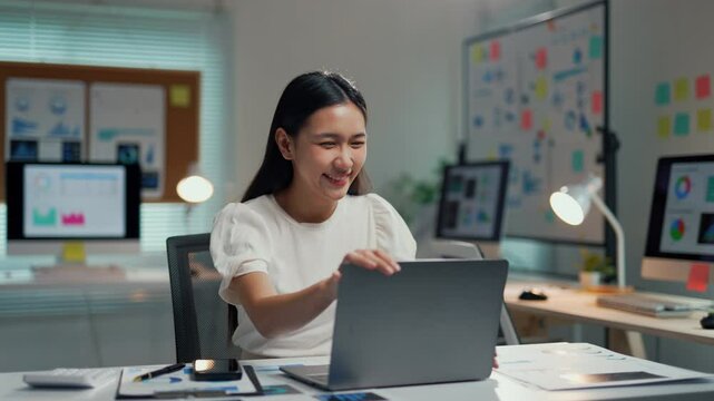 Asian freelancer closing her laptop at a desk, feeling satisfied after completing her work for the day