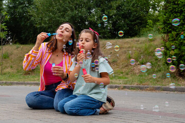 Young woman with her little girl playing with soap bubbles. Mother and daughter having fun together.