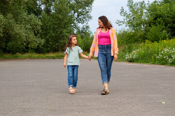 Obraz premium Young woman and her little girl are walking along the road. Mother and daughter are walking together.