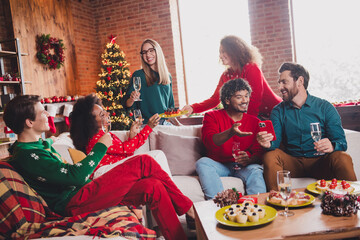 Photo of cheerful young people friends group sit couch communicate celebrate cozy christmas party decor spacious apartment indoors
