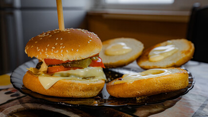 The finishing touches are being added to this delicious homemade burger. Pickles are placed atop the melted cheese, showing the care and precision that goes into making the perfect burger.