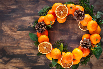 Wreath of fresh ripe tangerines with leaves and cones, on wooden background, top view