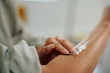 Close up of woman applying hydrating lotion on arm skin.