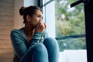 Ill woman blowing nose by  window.
