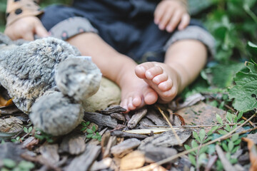 baby sitting next to a stuffed animal on ground grass wood chips and plants leaves 