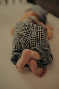 newborn baby laying on his stomach on ivory surface wearing grey black and white plad pants tiny feet 