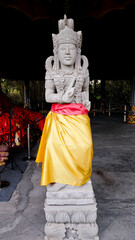 Sacred Balinese Hindu Stone Statue Draped in Yellow and Red Cloth in an Open Temple Setting