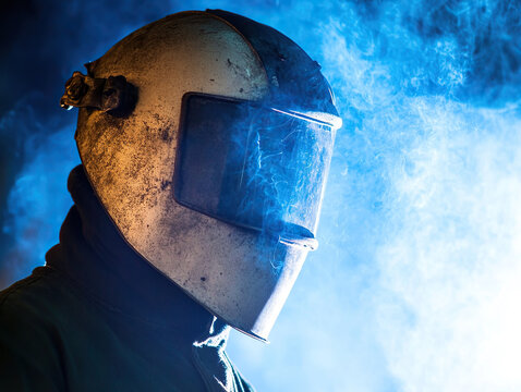 A welder with a protective mask fusing metal pieces together in a factory
