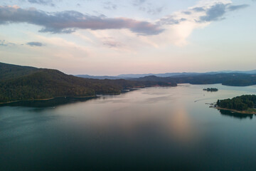 Fototapeta premium A serene view of a calm lake surrounded by lush green hills, reflecting the soft colors of twilight. A perfect escape for nature lovers and photographers alike.