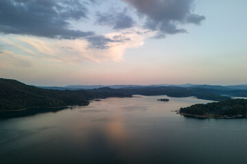 Fototapeta premium Aerial view of a tranquil lake surrounded by lush hills at sunset, showcasing beautiful reflections on the water's surface