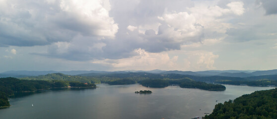 A stunning aerial view of a tranquil lake surrounded by lush greenery under a dynamic sky with clouds.