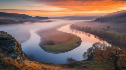 Obraz premium A tranquil river winding through misty hills during a colorful sunrise.