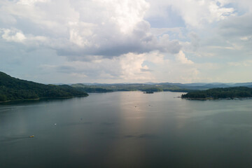 A serene view of a calm lake surrounded by lush green hills and an overcast sky, perfect for nature lovers and tranquility seekers.