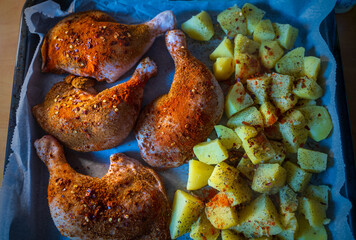 Seasoned chicken legs with paprika and herbs, paired with diced, spiced potatoes, ready to be roasted on a baking tray. A flavorful combination for a hearty and delicious meal.