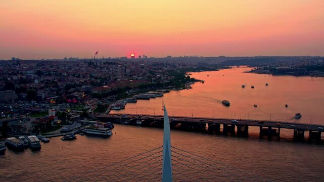 The video shows a panoramic view of Istanbul at sunset, featuring the Hali&ccedil; Bridge with a metro crossing. Historical mosques and docked boats add to the serene yet dynamic cityscape along the water.