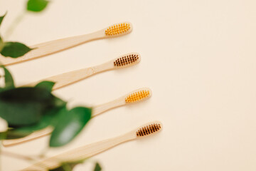 Eco friendly bamboo toothbrushes with green leaves on beige background, top view. Natural product,...