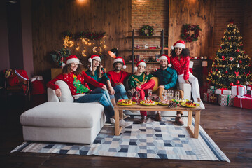 Full body photo of cheerful young people friends group sit couch celebrate cozy christmas party decor spacious apartment indoors