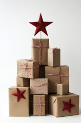 An aesthetic photo features Christmas gift boxes stacked in the shape of a tree, wrapped in brown kraft paper and tied with red or green twine against an white background.