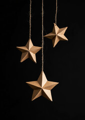 Star-shaped cardboard decorations hang against a black background in a close-up view.Minimal creative Christmas holiday concept.Copy space,flat lay