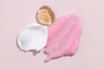 Composition of various cosmetic scrub, creams and serum smear on a pink background. Beauty texture....