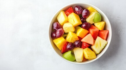 A bowl of organic mixed fruit salad including pineapple, grapes, and melon on a white table