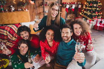 Photo of cheerful young people friends group sit couch drink champagne celebrate cozy christmas party decor spacious apartment indoors