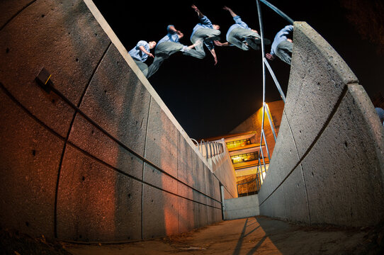 A male parkour athlete jumps a big gap at night in an urban setting in a multiple exposure. 