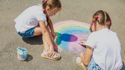 Girls drawing rainbow on sidewalk with chalk