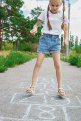 Little child playing hopscotch drawn with chalk on asphalt