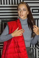 Young woman in red quilted down vest poses gracefully on creative striped background.
