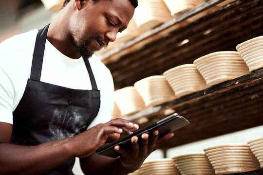 Worker, tablet and baker in factory for manufacturing, inventory storage and track order online. Bakery, black man or technology for food production, quality inspection or low angle in small business