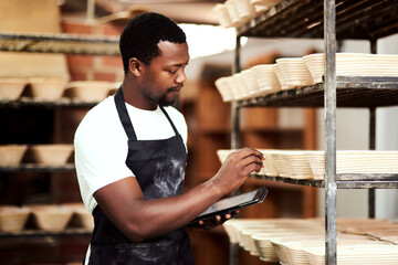 Black man, tablet and baker check stock, inventory or bread proofing basket on shelf. Technology, bakery and chef in factory for manufacturing, food production or quality inspection in small business