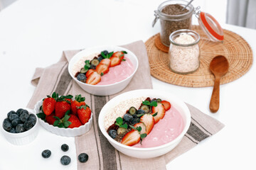 Presented by fruits putting yogurt toppings with strawberry, berry, oats, raisins and chia seed decorated by peppermint in white blow. Pink background. Set of healthy dairy product choice. Pecuniary.