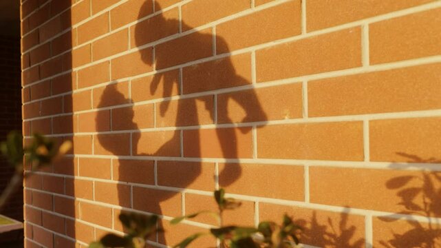 Father and son playing at sunset with the shadow on the wall made of orange bricks. Dad and Son emotional play with the sun before going to bed. Father builds a bond with his little child playing