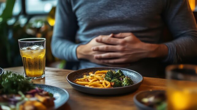 A man sits at a restaurant table with his hands on his stomach. He's wearing a grey shirt and there's a plate of food, a glass of iced tea, and other plates in front of him. - Powered by Adobe