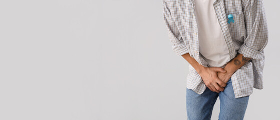 Young man with blue ribbon on light background, closeup. Prostate cancer awareness concept