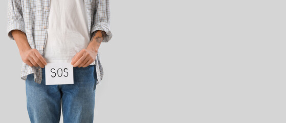 Young man holding paper with word SOS on light background, closeup. Prostate cancer awareness...