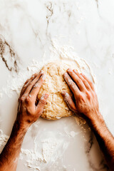 Hands kneading dough on a floured marble surface, top view of the baking process with focus on the texture of the dough and flour