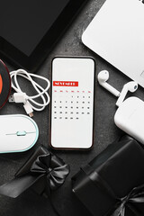 Mobile phone with calendar for November 2023, gift boxes and different devices on dark background....