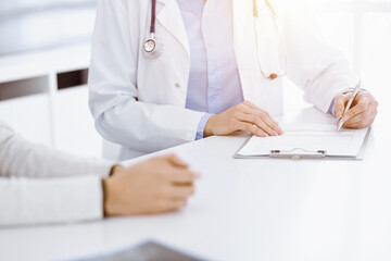 Unknown woman-doctor and female patient sitting and talking at medical examination in sunny clinic, close-up. Medicine concept