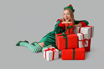 Young woman in elf costume with Christmas gift boxes on white background