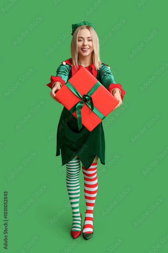 Canvas Prints Young woman in elf costume holding Christmas gift box on green background