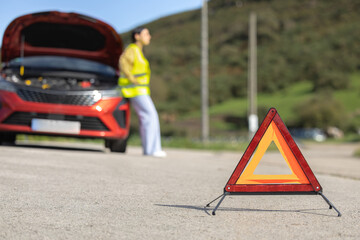 Pretty young woman poses in closeup placing emergency triangle sign and reflective vest on the...